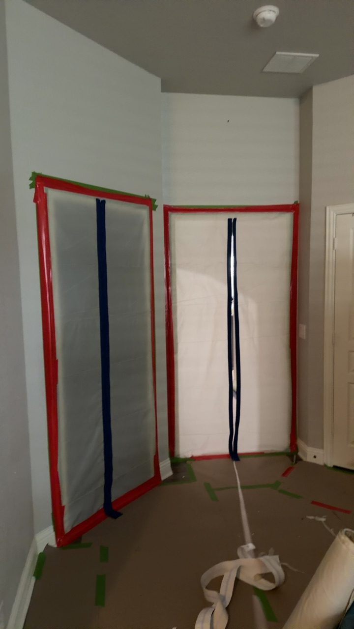 Interior containment set in a Southlake home after a burst pipe, with red poly zipper barriers sealing affected rooms and green tape marking the clean work zone