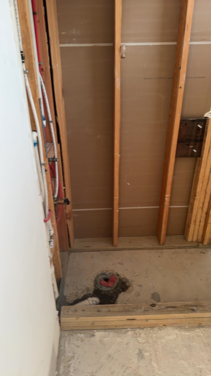 Utility alcove opened to bare studs after a supply line leak, with PEX water lines and a floor drain stub exposed.