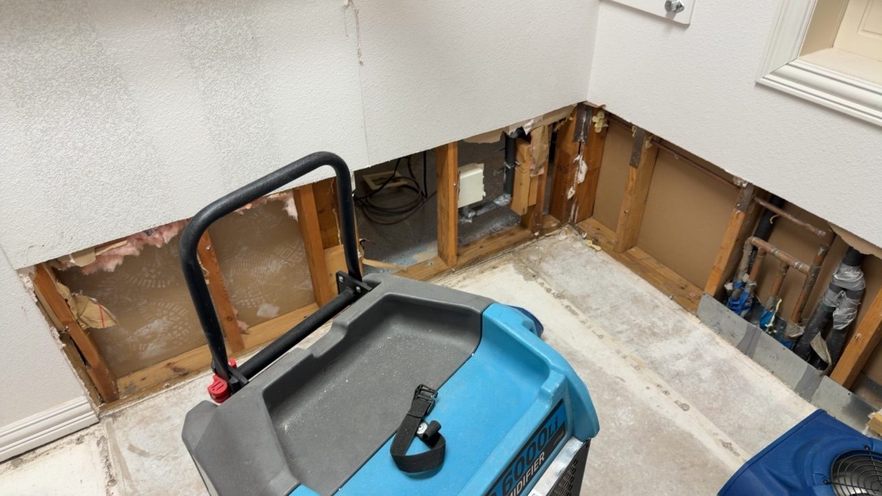 Flood cut at the base of a wall in a Southlake home after a water loss, saturated drywall and insulation removed, copper supply stub-outs exposed, refrigerant dehumidifier staged for structural drying
