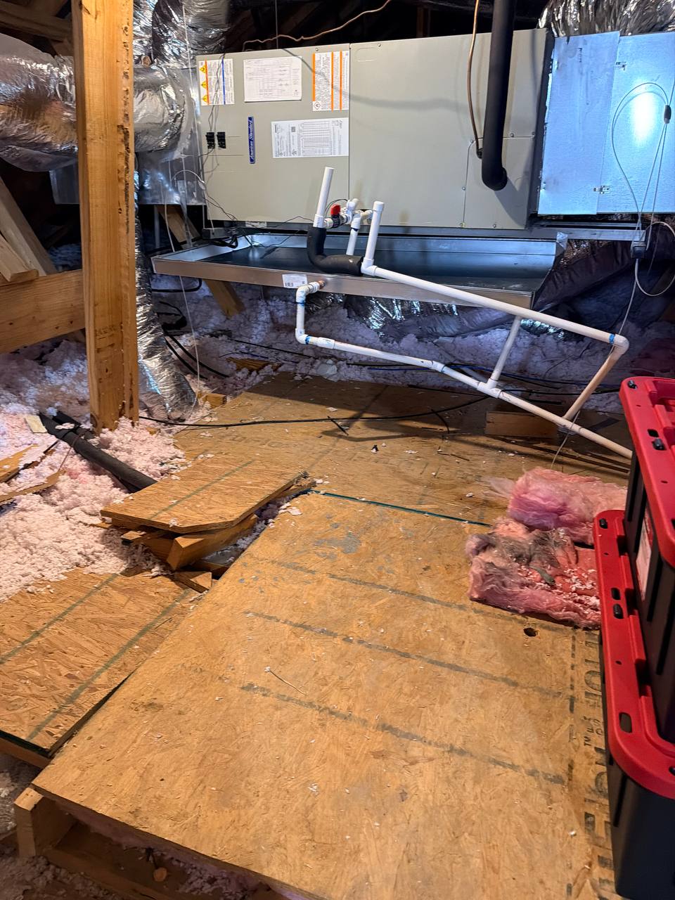 Attic air handler in a DFW home with the secondary metal drain pan visible underneath, surrounded by disturbed fiberglass insulation and water-stained OSB decking after a condensate overflow.