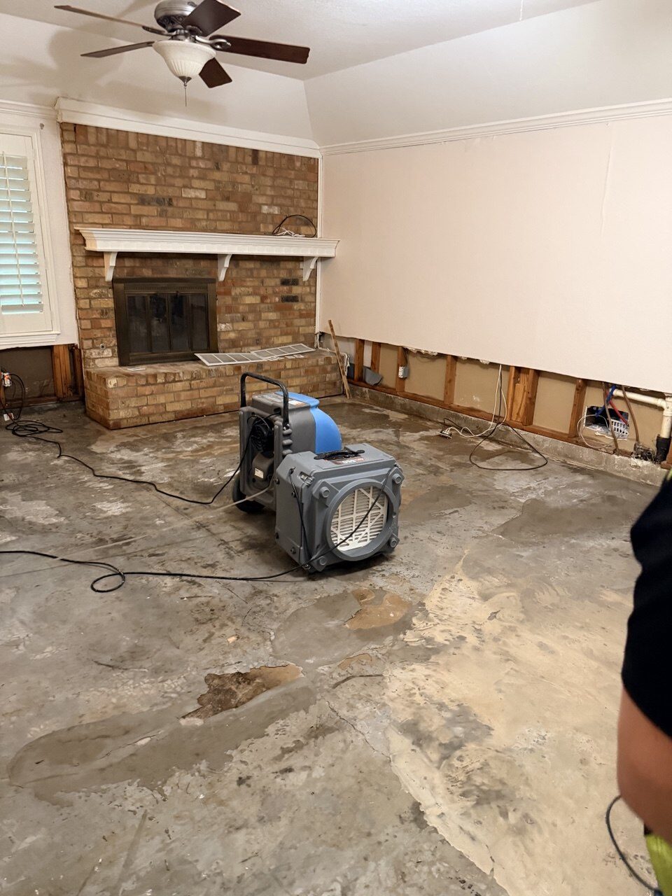 Family room with a floor-to-ceiling brick fireplace and a low-grain refrigerant dehumidifier stacked with an axial air mover running on the bare concrete slab